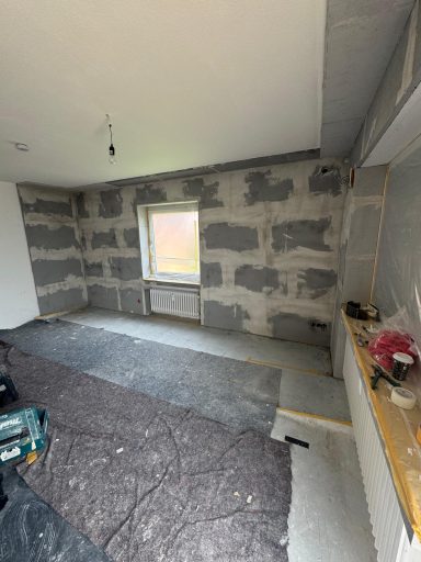 Rohbau eines Raums mit grauen Wänden und einem Fenster, Parkettboden und unvollständiger Ausstattung.